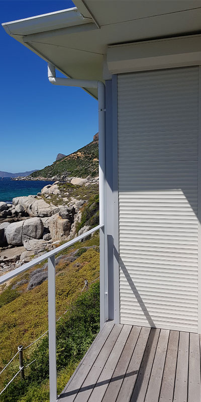White roller shutter on a coastal deck overlooking rocky shoreline and ocean