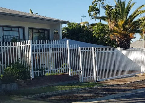 White palisade fencing and sliding gate outside a house with palm trees
