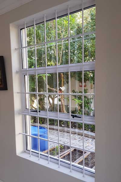 White grid-pattern grille with courtyard view of greenery