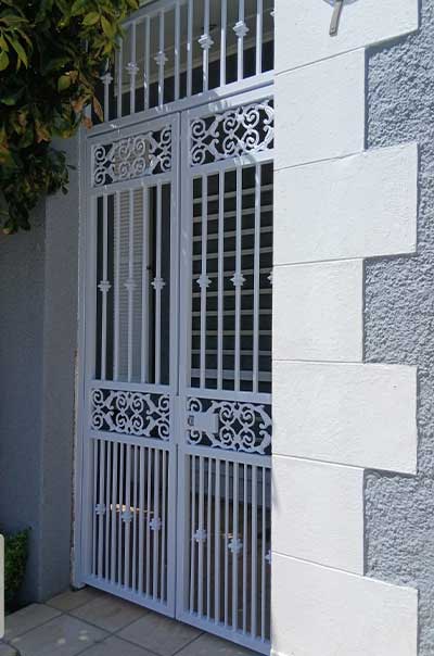 Ornate white double gate with scrollwork panels beside a stone brick wall