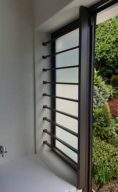 Black horizontal slat grille on a side opening beside a green garden bed