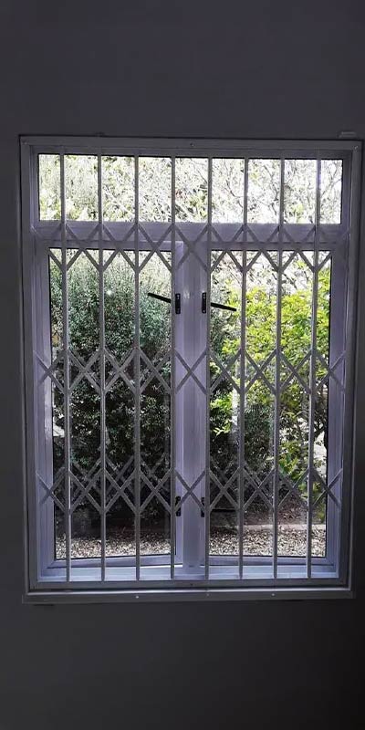White diamond-pattern security grille on a tall opening with garden shrubs beyond